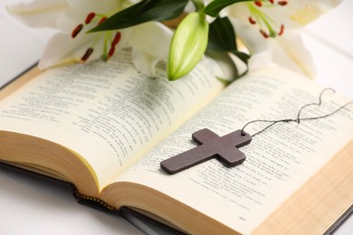 Cross, Bible and beautiful lily flowers on white table, closeup. Religion of Christianity