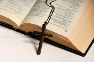 Cross with chain and Bible on white wooden table, closeup. Religion of Christianity