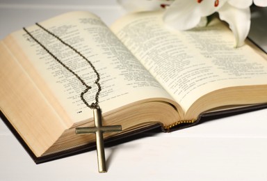 Photo of Cross with chain and Bible on white wooden table, closeup. Religion of Christianity