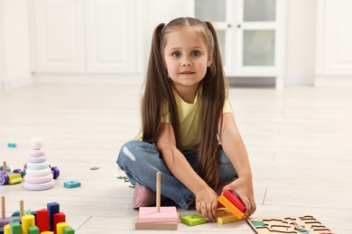 Photo of Cute little girl playing with toy pyramid on floor indoors