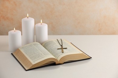 Photo of Cross with chain, burning candles and Bible on white table. Religion of Christianity