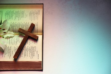 Wooden cross, Bible and lily flower on textured table in color lights, top view with space for text. Religion of Christianity