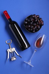 Photo of Wing corkscrew, wine, grapes and glass on blue background, flat lay