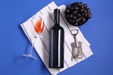 Photo of Wing corkscrew, wine, grapes and glass on blue background, flat lay