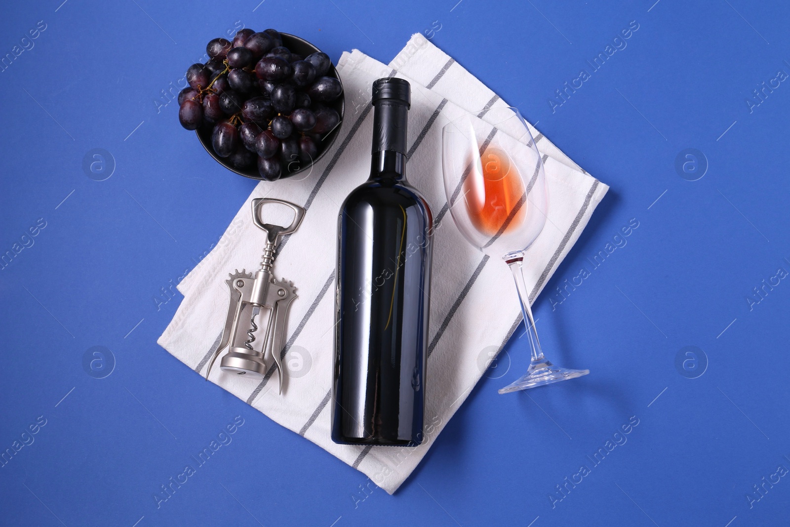 Photo of Wing corkscrew, wine, grapes and glass on blue background, flat lay