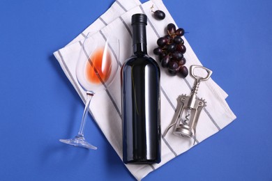 Photo of Wing corkscrew, wine, grapes and glass on blue background, flat lay