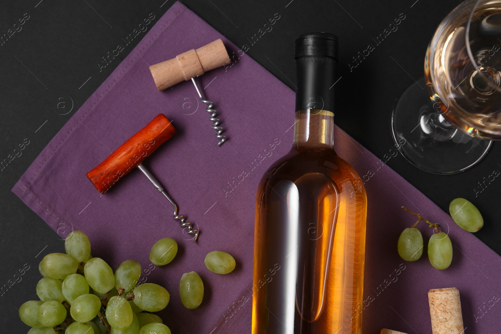 Photo of Corkscrews, wine and grapes on black background, flat lay