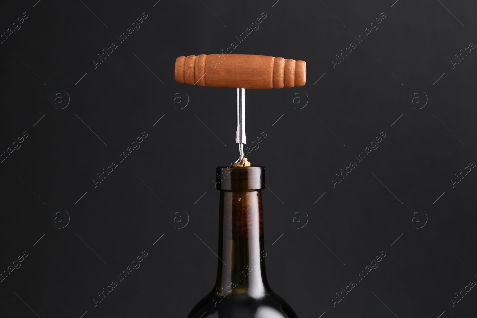 Photo of Wine bottle with corkscrew on dark background, closeup