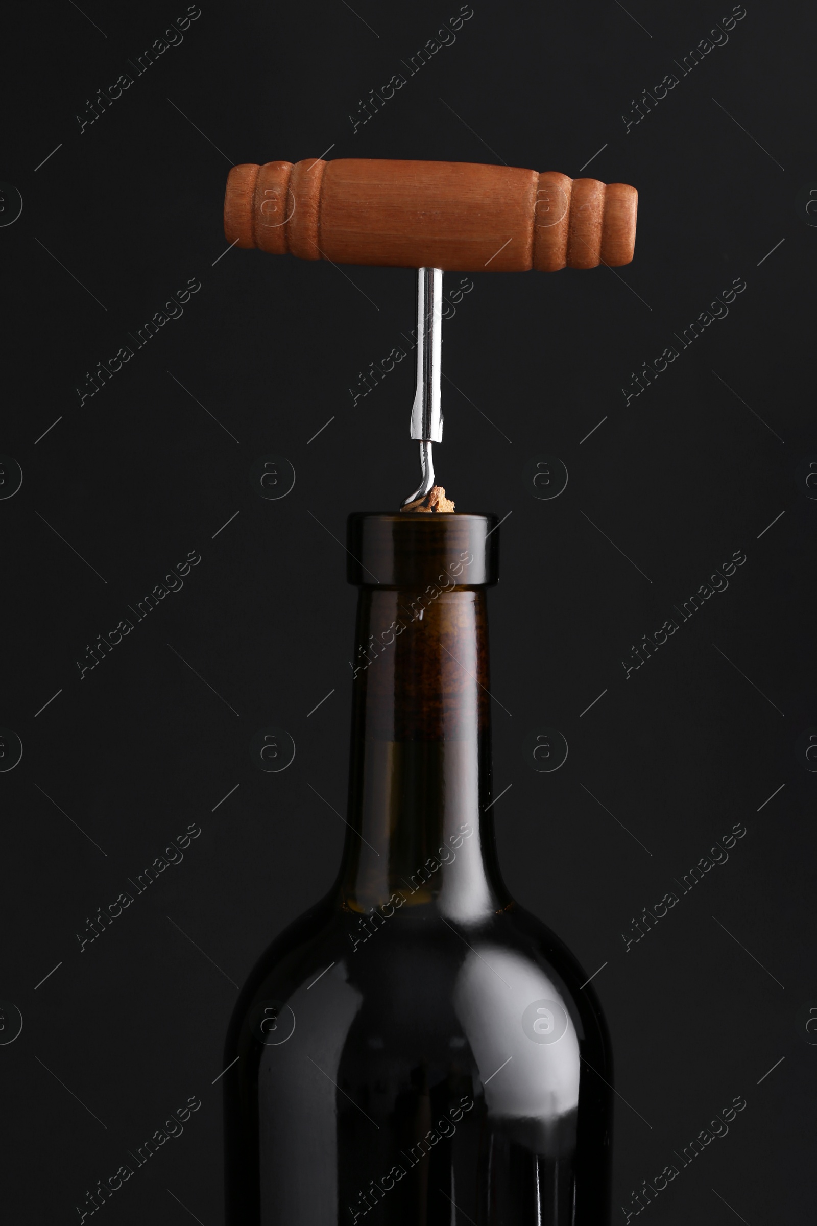 Photo of Wine bottle with corkscrew on dark background, closeup