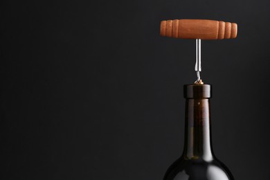 Photo of Wine bottle with corkscrew on dark background, closeup. Space for text