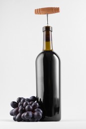 Wine bottle with corkscrew and fresh grapes on grey background