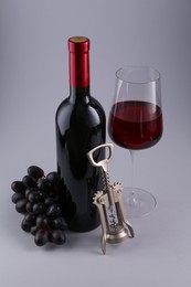 Red wine, wing corkscrew and fresh grapes on grey background