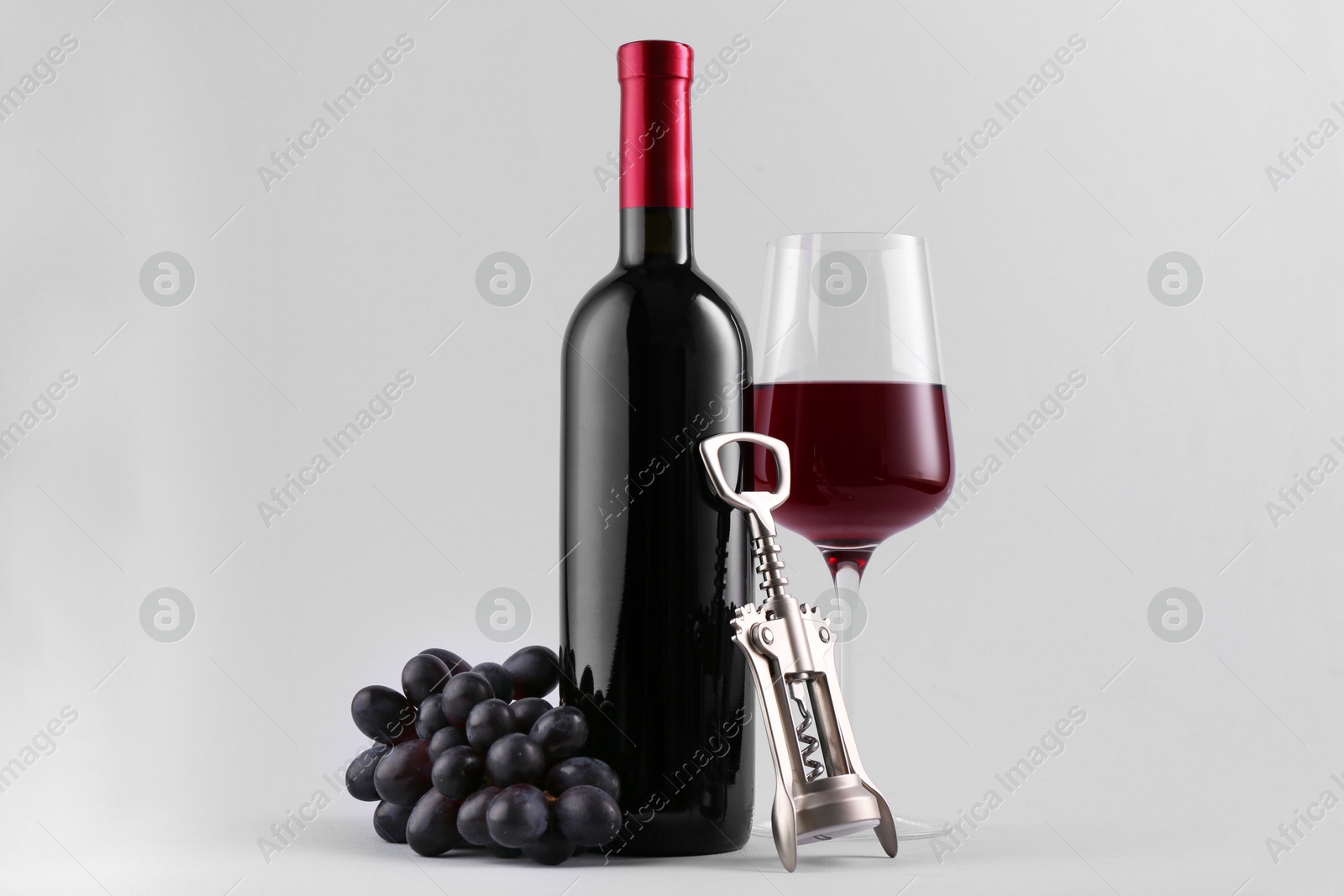 Photo of Red wine, wing corkscrew and fresh grapes on grey background