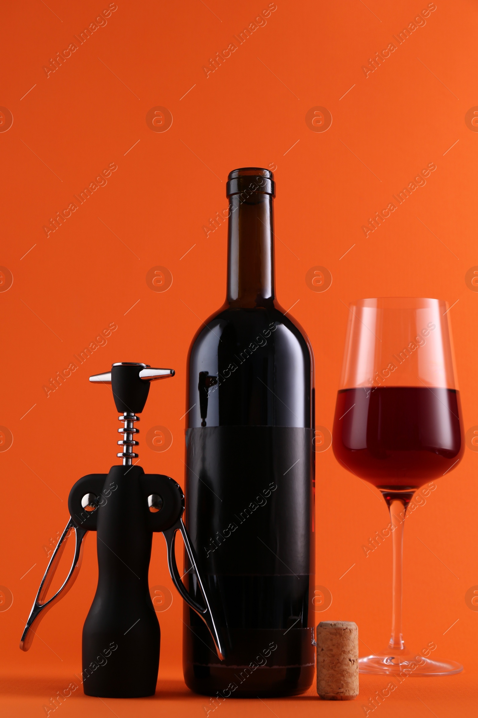 Photo of Wing corkscrew, red wine and cork on orange background