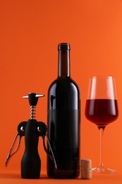 Wing corkscrew, red wine and cork on orange background