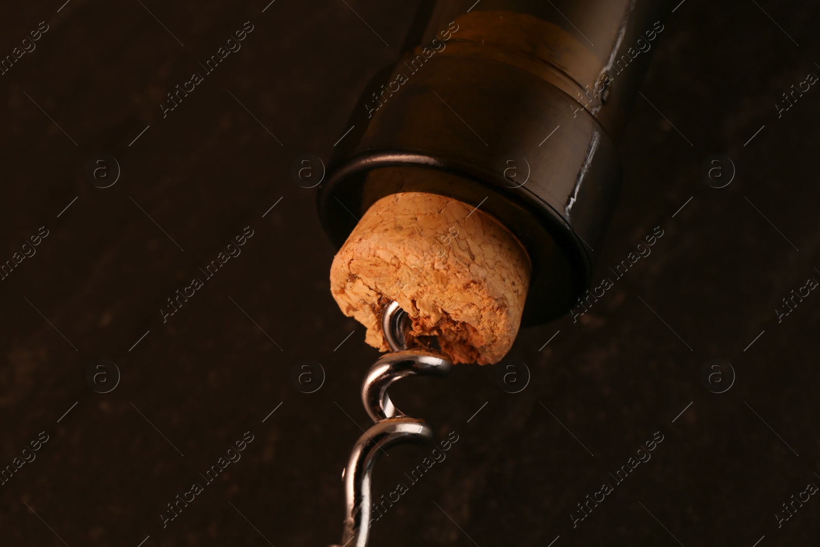 Photo of Wine bottle with corkscrew on dark background, closeup