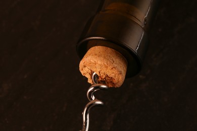 Wine bottle with corkscrew on dark background, closeup