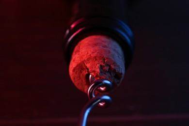 Photo of Wine bottle with corkscrew in lights on table, closeup