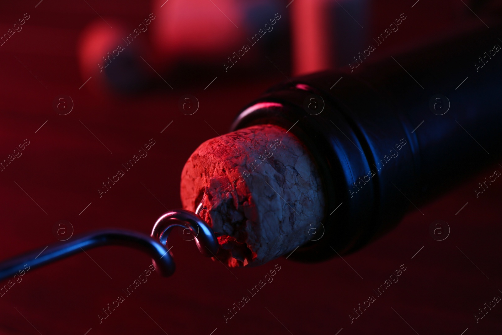 Photo of Wine bottle with corkscrew in lights on table, closeup