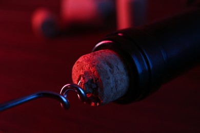 Wine bottle with corkscrew in lights on table, closeup