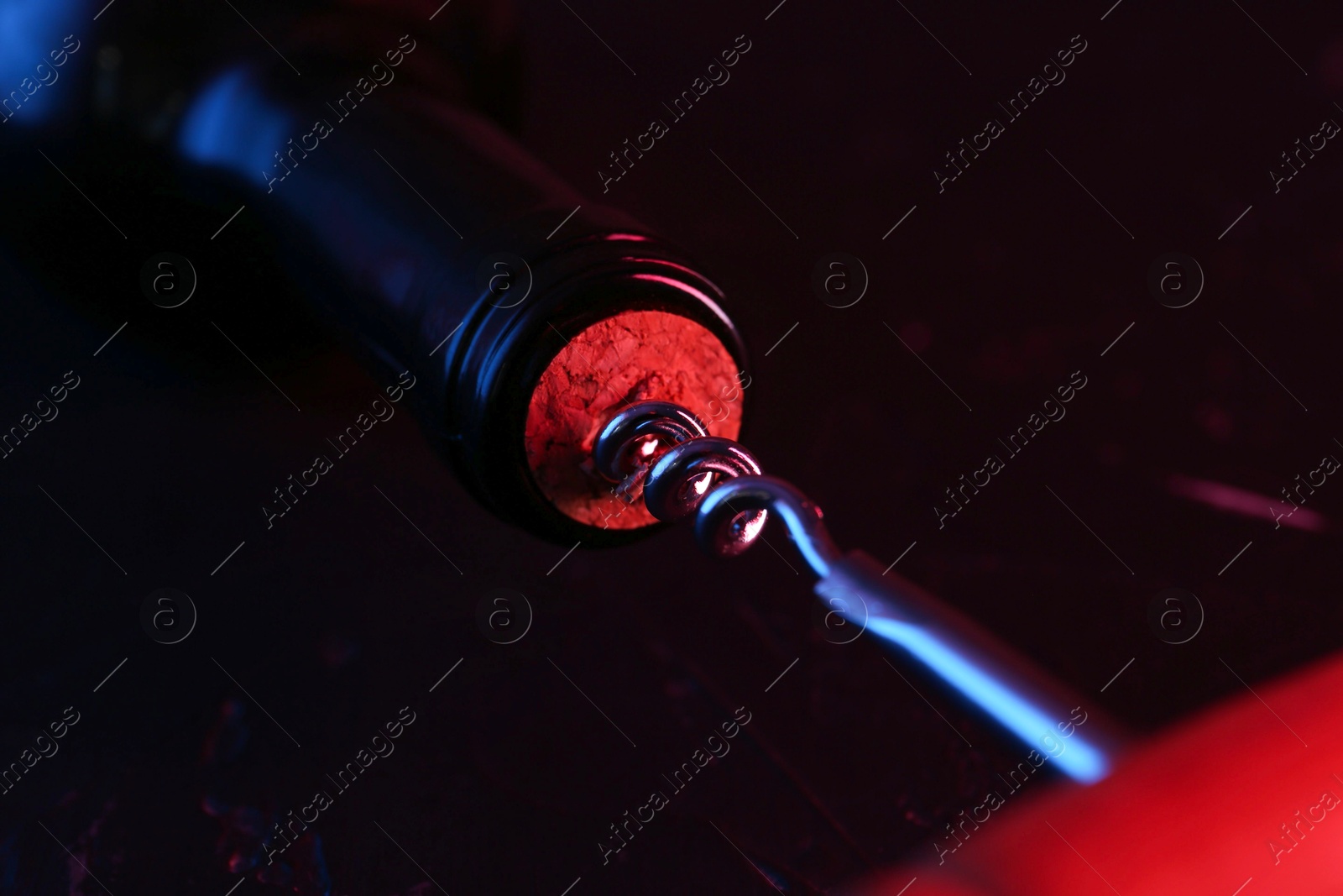 Photo of Wine bottle with corkscrew in lights on dark background, closeup