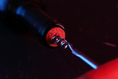 Wine bottle with corkscrew in lights on dark background, closeup