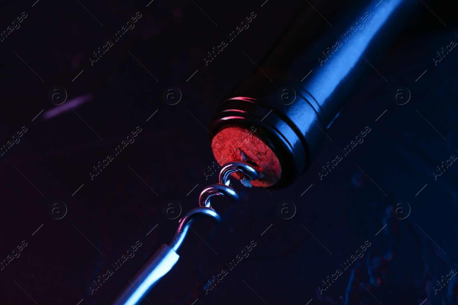 Photo of Wine bottle with corkscrew in lights on dark background, closeup