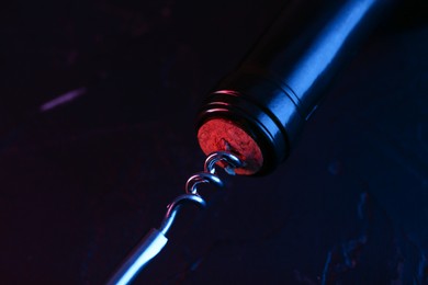 Photo of Wine bottle with corkscrew in lights on dark background, closeup