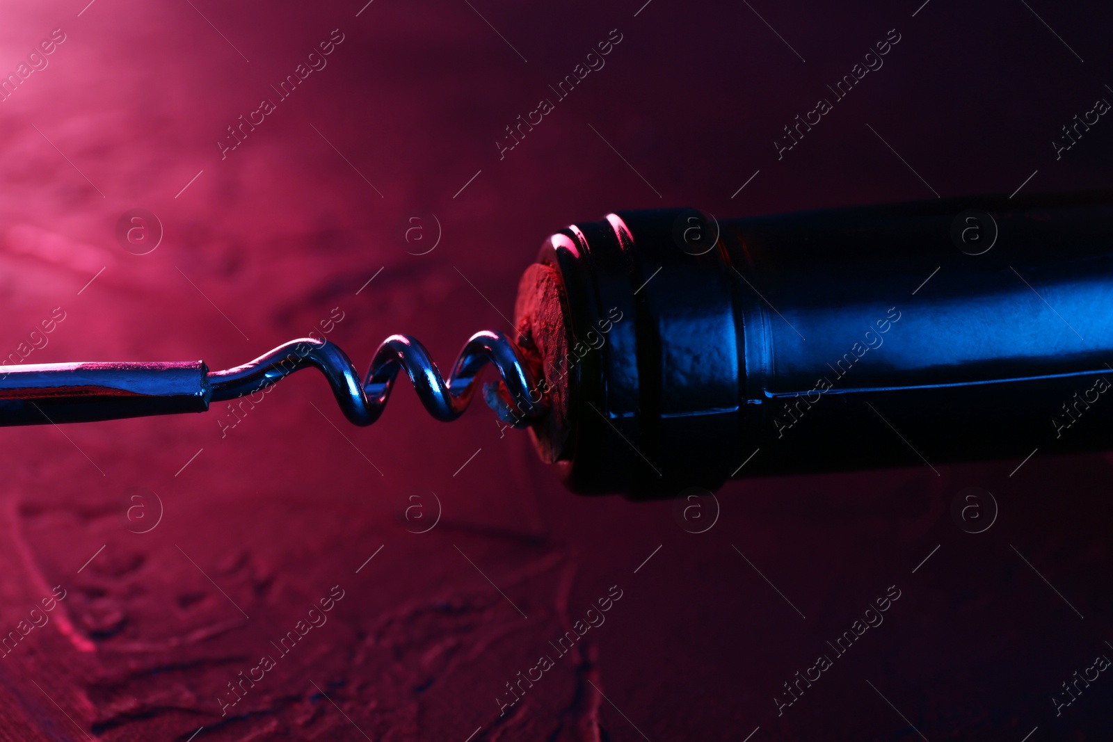 Photo of Wine bottle with corkscrew in lights on table, closeup