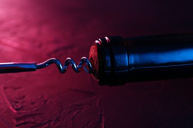 Photo of Wine bottle with corkscrew in lights on table, closeup