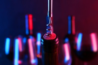 Wine bottle with corkscrew in lights on blurred background, closeup