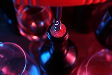 Photo of Wine bottle with corkscrew in lights on table, closeup