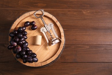 Photo of Wing corkscrew, cork, grapes and barrel on wooden table, top view. Space for text