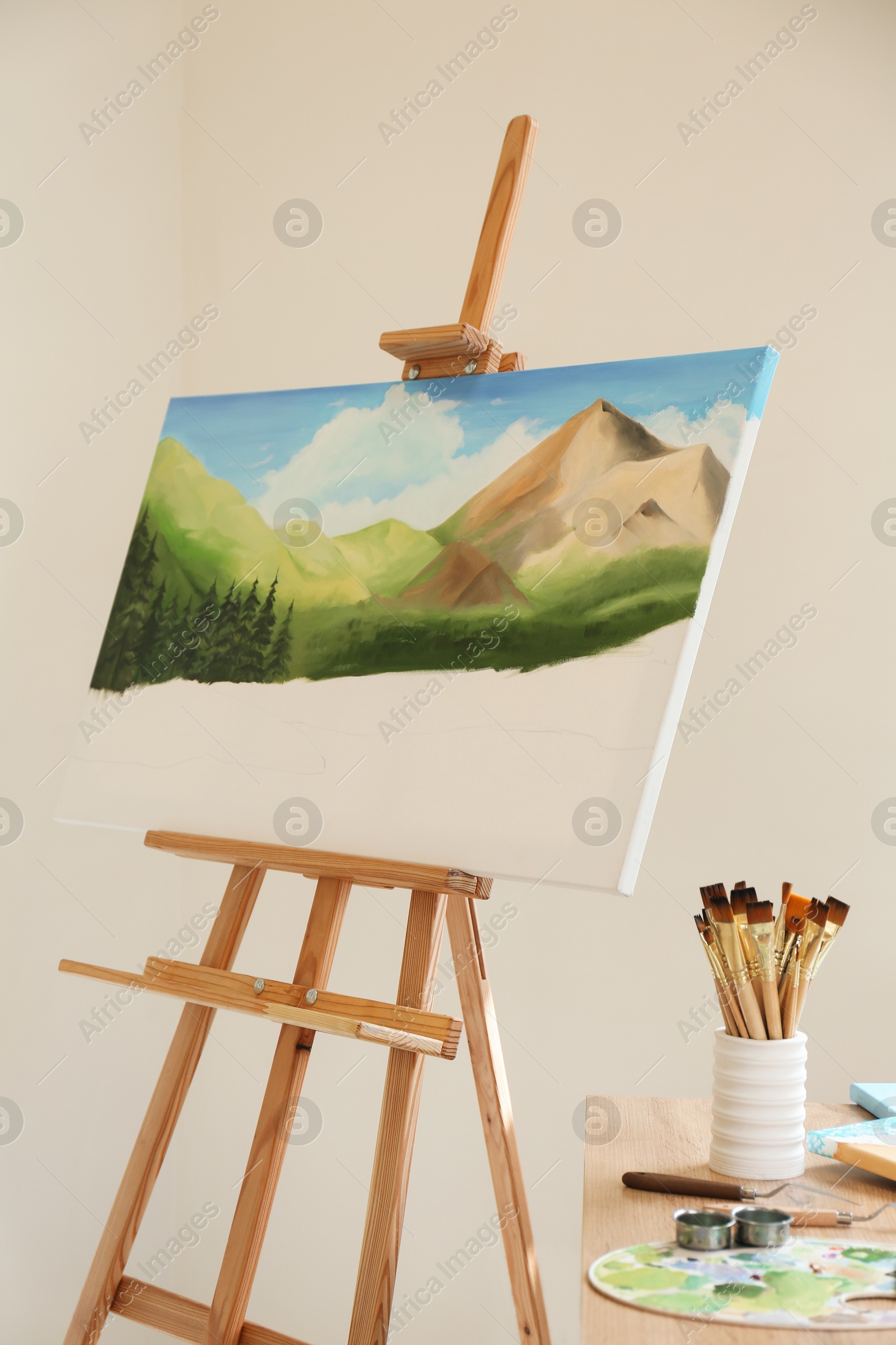 Photo of Easel with beautiful landscape in drawing studio. Unfinished artwork