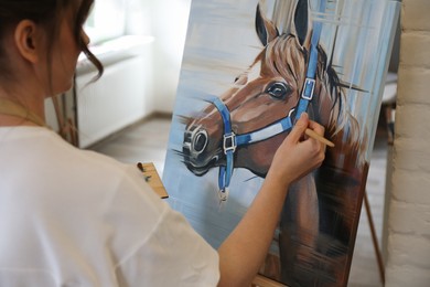 Photo of Woman drawing cute horse with brush in studio, closeup