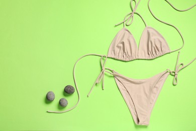 Beige swimsuit and stones on green background, flat lay. Space for text