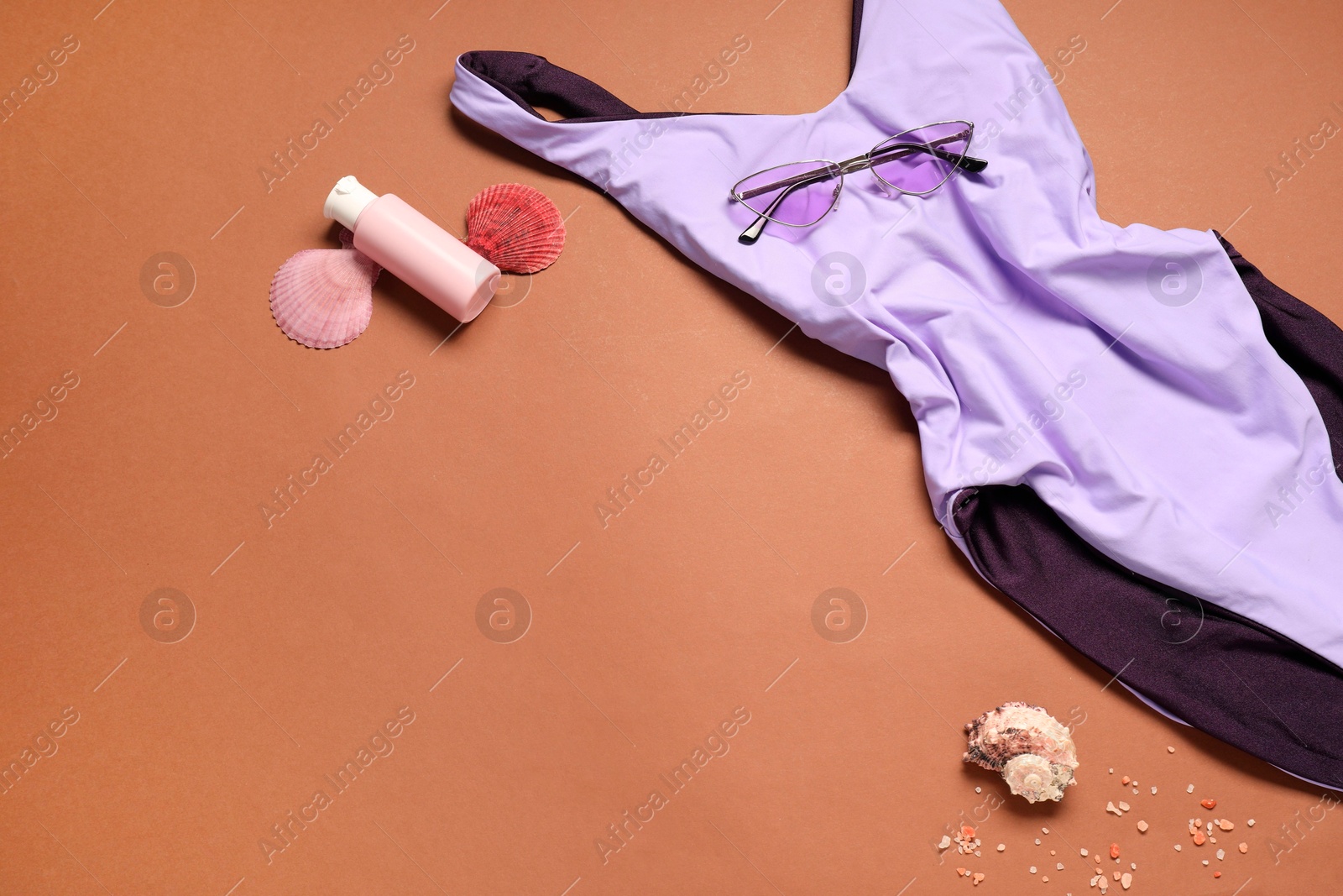 Photo of Violet swimsuit, sunglasses, sunscreen and seashells on brown background. Space for text