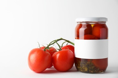 Tasty pickled tomatoes in jar and vegetables on light background, closeup. Space for text