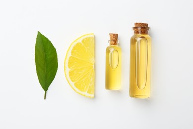 Bottles of essential oils, lemon and green leaf on white background, flat lay