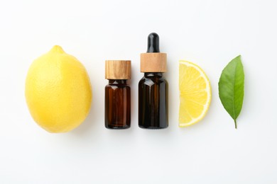 Bottles of essential oils, lemon and green leaf on white background, flat lay