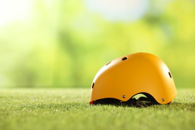 Yellow protective helmet on green grass, space for text