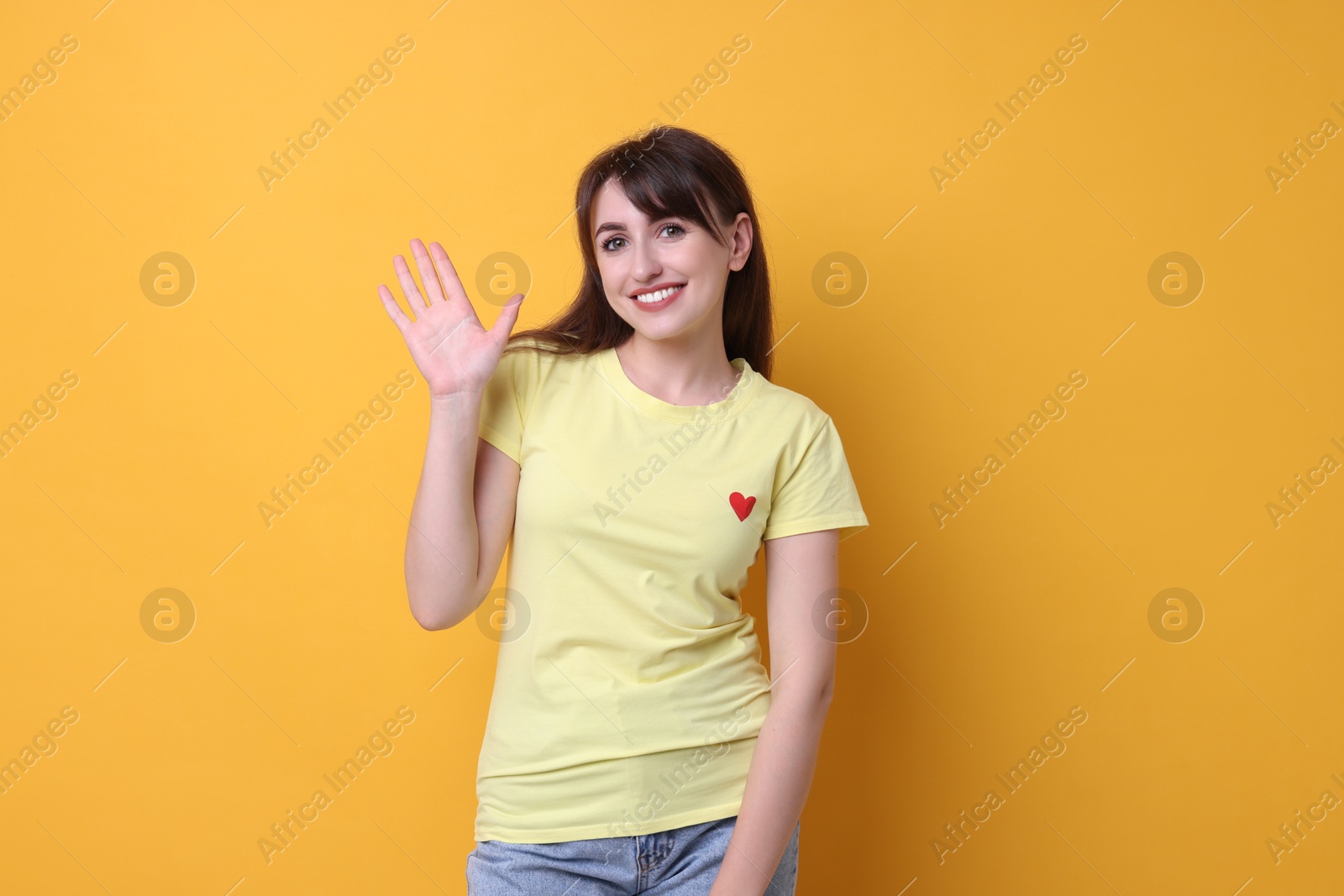 Photo of Happy young woman waving on orange background