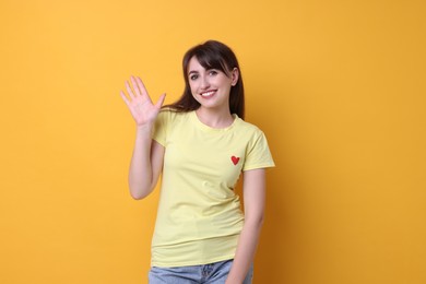 Happy young woman waving on orange background