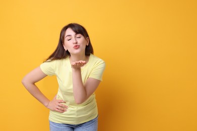 Photo of Beautiful woman blowing kiss on orange background, space for text