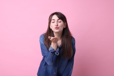 Beautiful woman blowing kiss on pink background