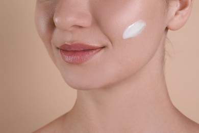 Photo of Woman with cream on her face against beige background, closeup