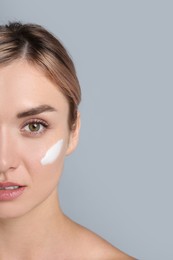 Beautiful woman with cream on her face against gray background, closeup