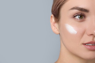 Beautiful woman with cream on her face against gray background, closeup. Space for text