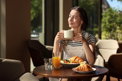 Photo of Happy woman having tasty breakfast in cafe, space for text