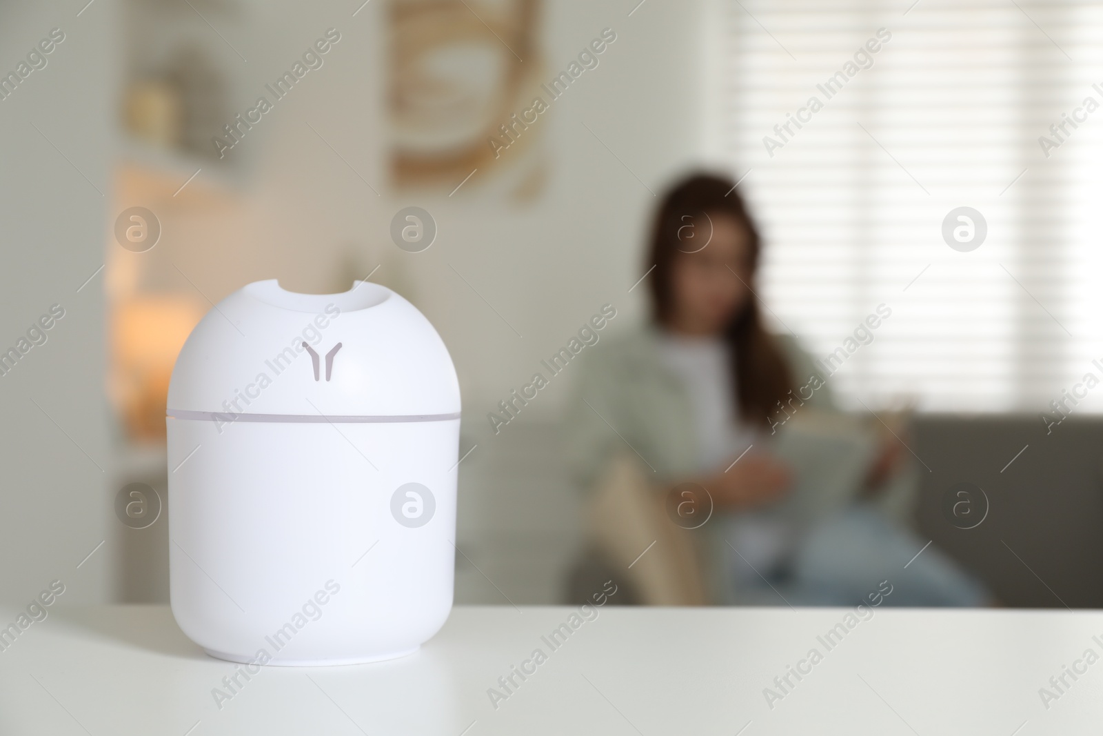 Photo of Woman reading book at home, focus on essential oil aroma diffuser